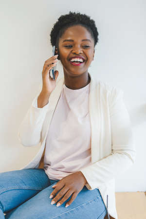 Beautiful African woman standing on the windowsill of a bar talking on the phone with her friends,...