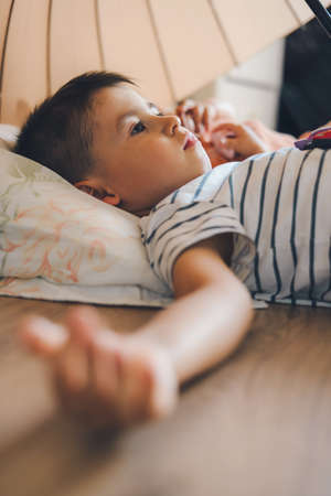 Adorable boy lying on his back on the playroom floor under the umbrella with his sister to put her to sleep. People lifestyle concept. Childhood concept. Health insurance concept.の写真素材