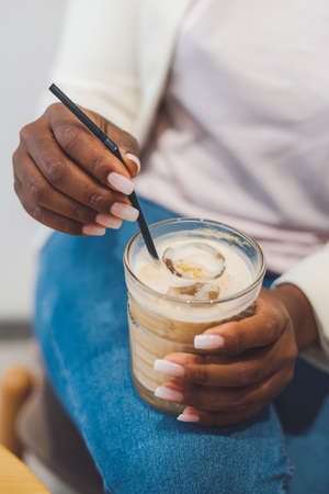 Close-up portrait of womans hands holding glass of iced coffee with ice cubes. Tasty Iced coffee. Summer drinksの写真素材