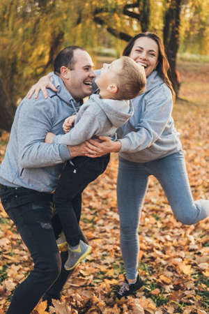 Happy family of three members resting in autumn city park posing against the beautiful yellow trees. Happy family outdoors. Activity relationship. Parent, child. Happy family, childhood.の写真素材