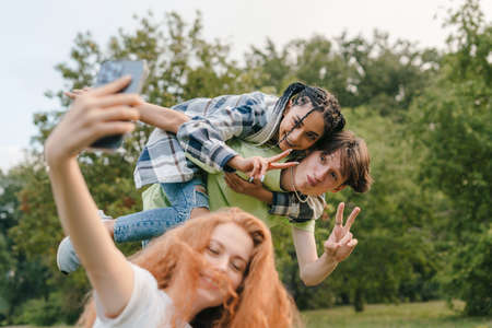 Ginger beautiful girl using smartphone taking crazy selfie outdoor, with her two friends making faces. New generation technology. City lifestyle.の写真素材