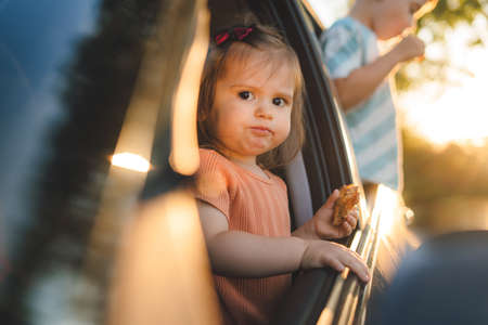 Two children sticking their heads out of windows of a car looking forward for a road trip or travel. Road trip concept. Summer vacation fun.の写真素材