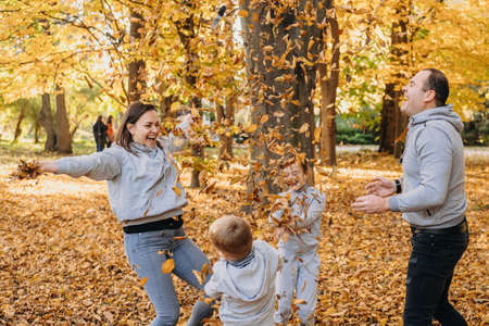 Portrait of a family with children tossing autumn leaves in park in autumn. Family portrait of four members, father, mother and children. Family concept.の写真素材