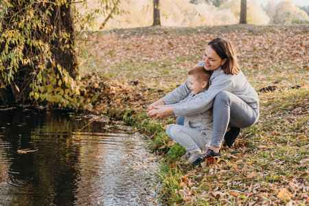 The mother playing with her son on the edge of a lake imitating fishing a big and heavy fish with a rod. Natural forest landscape. Natural beauty. Beauty portrait. Mother nature.の写真素材