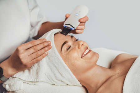 Beautician squeezing acne on the patients forehead with a medical needle. Dermatology, cosmetology. Cleaning concept. Beauty treatment. Beauty, skincare. Medical health.の写真素材