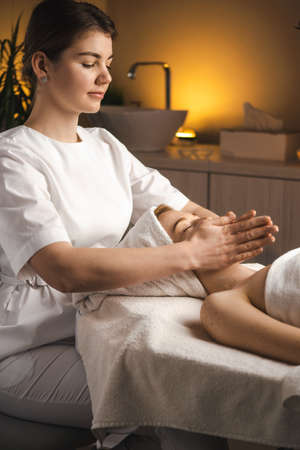 Masseur therapist doing rejuvenating facial massage procedure in a beauty salon. Skin care. Body care. Woman doctor portrait.の写真素材