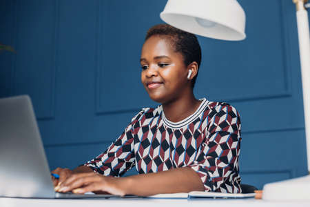Beautiful Afro woman sitting at office desk using laptop computer for browsing the internet....