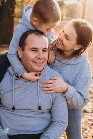 Caucasian little boy sitting on his fathers shoulders being on a walk with the family in autumn park having fun. Outdoor photo in autumn park. Sunset light raysの写真素材