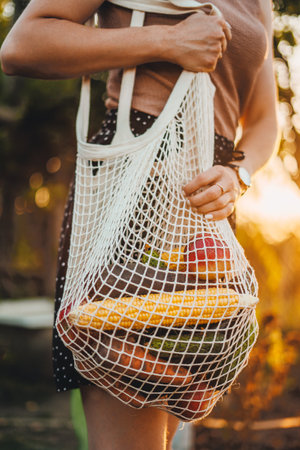 Cropped view of a woman farmer carrying a net bag with various vegetables. Harvesting. Autumn. Zero waste concept. Concept of sustainability and organic homegrown foodの写真素材