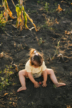 Top view of a playful girl burying a tomato in the ground. Beautiful caucasian child girl farmer resting enjoy fun playing in backyard. Happy family, childhood.の写真素材