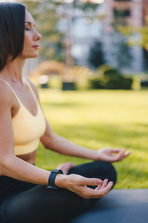 Side view of a woman in sportswear practicing meditation in a urban park sitting in lotus position on her yoga mat. Fitness woman. Healthy lifestyle, sport. Active healthy lifestyle. Fitness workout.の写真素材
