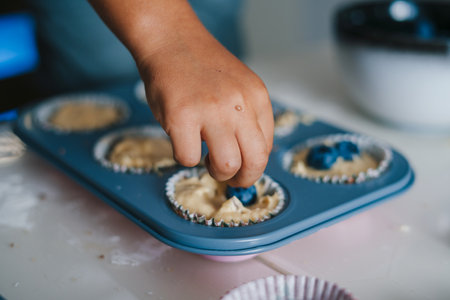 A boys hand putting blueberries on the dough already divided into baking forms for the holiday...