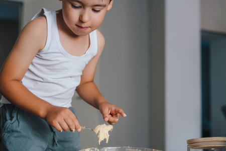 Caucasian boy pouring batter with spoon into the form for muffins spending time into the kitchen. Happy family in the kitchen. Bake cookiesの写真素材