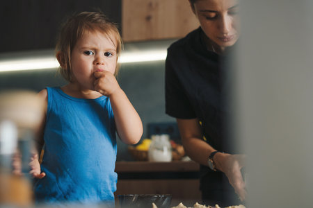 Adorable funny blond little baby girl baking chocolate cake and tasting dough in domestic kitchen. Happy family. Sweet food.の写真素材