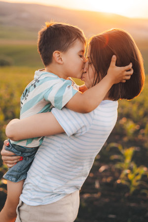 Profile portrait of a mother with her son kissing, having fun in corn field together at sunset. Happy family. Summer in corn. Happy childhood. Happy motherhood.の写真素材