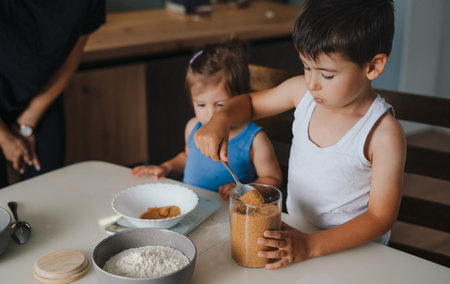 Caucasian little boy pouring the prepared cake mix into the bowl with the rest of the ingredients. Activities with children at home.Boy is fascinated by the process. People lifestyle food concept. Parent concept.の写真素材