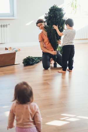Family portrait of three members assembling the Christmas tree in their living room. Parent, child. Happy family, childhood.の写真素材