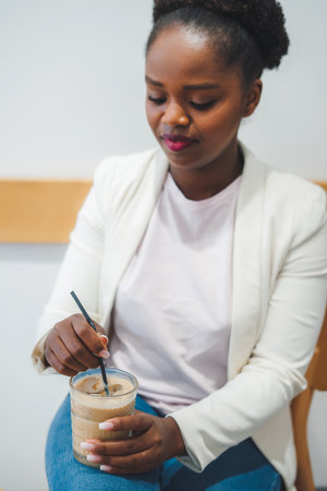 Young smiling african woman relaxing drinking latte coffee while sitting in the cafe shop, thinking and enjoying free time. Lunch break. Beauty portrait.の写真素材