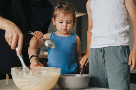 Mother teaching small adorable kids mixing flour with milk, cooking together in modern kitchen....