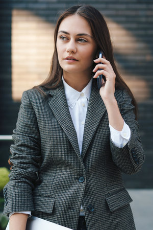 Portrait of an attractive caucasian woman talking on the phone, holding laptop, standing at cafe garden in the city. People lifestyle. Communication network.の写真素材