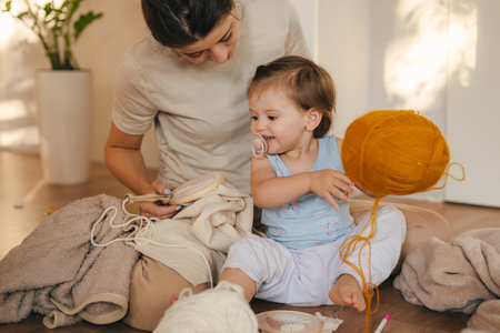Mother embroidering at the weekend with her younger daughter playing with colorful balls of thread. Needlework. Embroidery with satin and nylonの写真素材