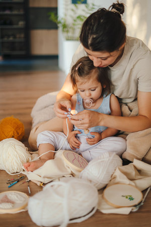 Pleasant smart woman sitting together with her daughter teaching her to embroider. Between generations. Parent, child. Creative design.の写真素材