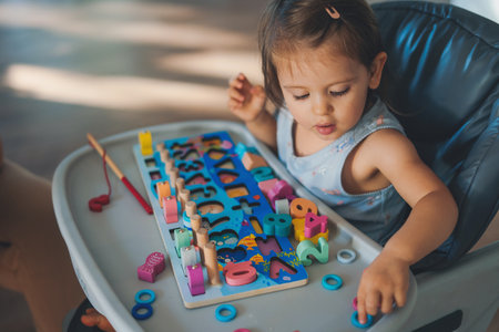 Shot of baby girl sitting on the high chair while learning and playing wooden toys at home. Infant in kindergarten. Colorful portrait. Baby development.の写真素材