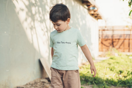 Sad child in a t-shirt playing in the garden outdoors, standing outside on a summer day. Carefree childhood concept. Summer nature.の写真素材