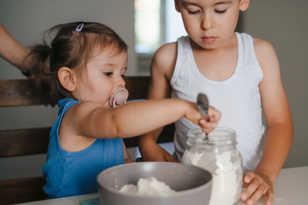 Two happy little kids preparing muffins at modern kitchen at home, weighing how much flour is needed for their recipe. Fun family.の写真素材