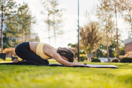 Side view of a woman in comfy activewear, resting performing relaxation exercise, and stretching lower back. Outdoor lifestyle. Healthy lifestyle, sport. Fitness workout. Healthy active lifestyle.の写真素材