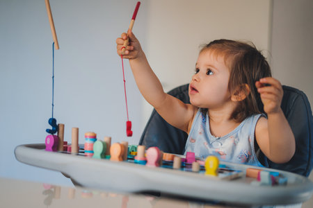 Funny cute Caucasian baby girl sitting on high chair and playing with educational wooden toy. Colorful portrait. Baby development.の写真素材