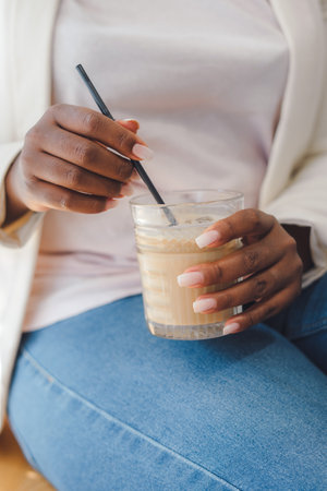 The hands of an American woman holding a latte glass and a straw. Free time weekend activities concept. Small business coffee shopの写真素材