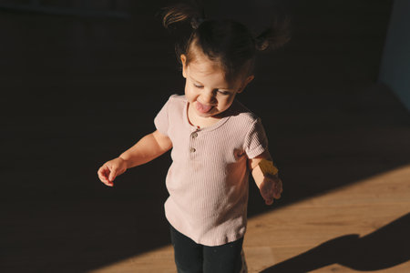 The baby girl playing around the house with a biscuit in her hand that she is enjoying, surrounded by darkness. Concept of childhood. Fun family.の写真素材