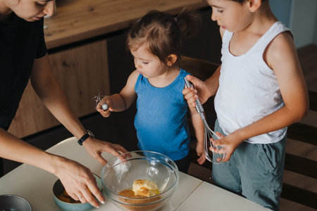 Adult woman and two cute kids adding ingredients into bowl with dough while cooking pastry at home together. Attractive beautiful girl. Parent, child. Happy family.の写真素材
