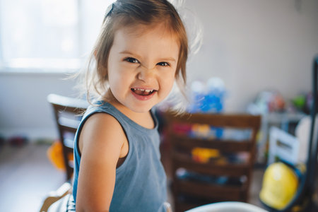 Closeup portrait of cheerful cute little girl sitting at table in kitchen, relaxing at home, looking at camera and smiling. Kitchen interior. Smiling happy child. Beauty portrait.の写真素材