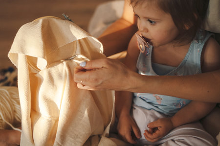Baby girl sucking a pacifier sitting on the floor and watching her mother embroider. Between generations. Home decoration. Closeup portrait.の写真素材