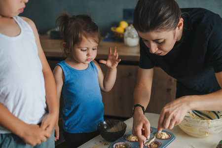 Mother spooning raw dough into baking pans to make birthday cakes. Happy family. Smiling happy...