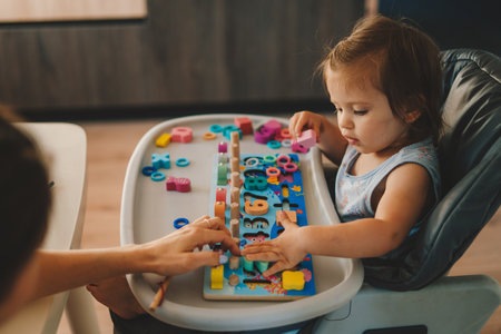 Mother with her baby girl sitting at the table, studying number and colors together. Educational...