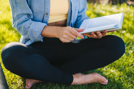 Cropped view of woman's hands holding an open book relaxing in a park in the summer. Relax, lifestyle concept. Summer relaxation concept. Healthy lifestyle concept. Healthy lifestyle, sport. Fitness woman.の写真素材
