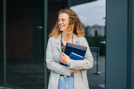 Portrait of a young female student with books and laptop going from the university after lecture, walking on the street. People and urban lifestyle conceptの写真素材