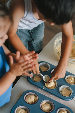 Little child pouring homemade fresh raw dough into baking forms for baking bakery cakes at home...