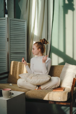 Woman sitting on sofa at cozy room having fun while applying moisturizing cream on her face. Morning higiene routine at home.の写真素材