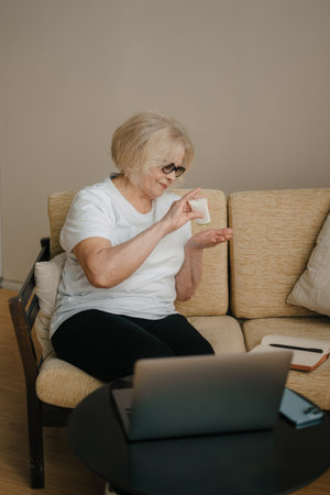 Gorgeous old woman opening tube of cream, applying cosmetic cream onto her hands, sitting on the...