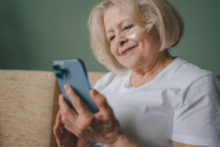 Old woman having a conversation on the phone through the video camera, sitting on the sofa. Mobile...