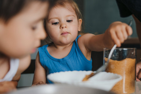 Adorable baby girl adding flour to the bowl with dough ingredients helping mother to prepare delicious muffins in the kitchen. Baking with children. Little happy kidの写真素材