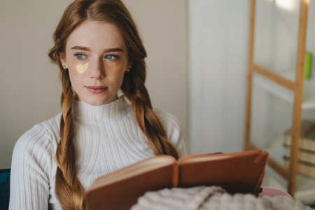Portrait of young woman working at home sitting on the sofa, writting a to-do list. Cozy apartment.の写真素材