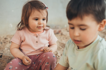 A cute baby girl with her brother playing with sand on playground in the weekends. Plays. Outdoor activities, joint pastime, recreation concept.の写真素材