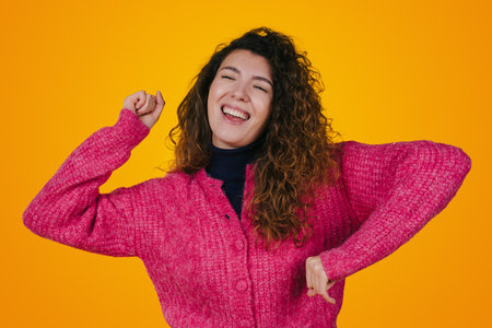 Excited woman dancing and whipping her curls while standing against yellow background. Happy woman...