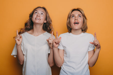 Happy screaming young women pointing and looking up with open mouths isolated over yellow background.の写真素材