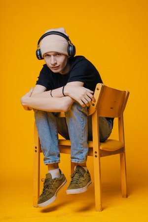 Relaxed man listening to music in wireless headphones, resting on chair isolated over yellow studio background. Happy man chilling and enjoying audio bookの写真素材